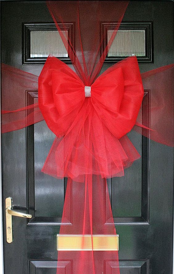 A black front door wrapped in a large red Christmas bow