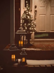 Small Christmas tree sitting on a front porch lit up at night