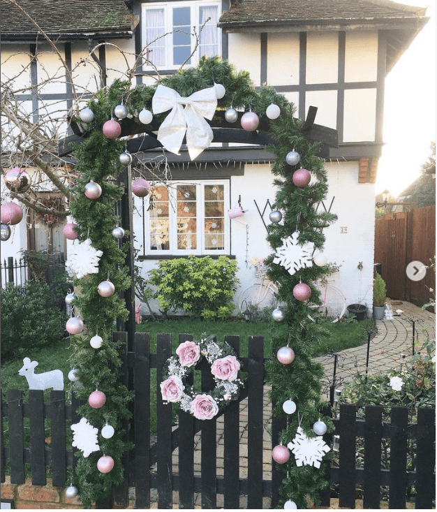 A decorated archway leading into a front garden featuring pink baubles and Christmas decor.