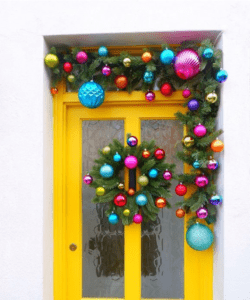 A yellow door surrounded in brightly coloured Christmas baubles