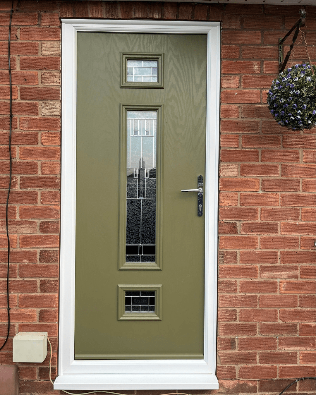 Green front door with three decorative glazed windows set in red brick wall